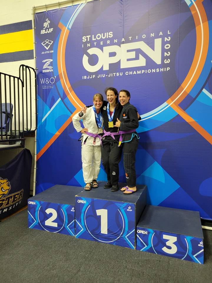 Three women with purple belts and medals on the podium at the 2023 St. Louis International Open, an IBJJF championship